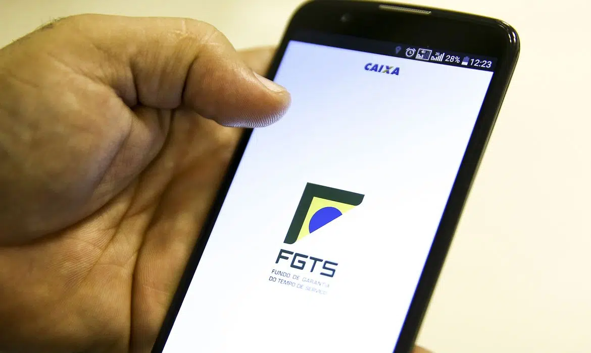 Foto de pessoa segurando celular com logo do aplicativo do FGTS na tela.