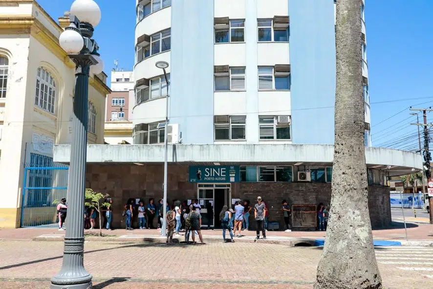 Imagem da fachada do Sine Municipal, com filas de pessoas buscando vagas de emprego.