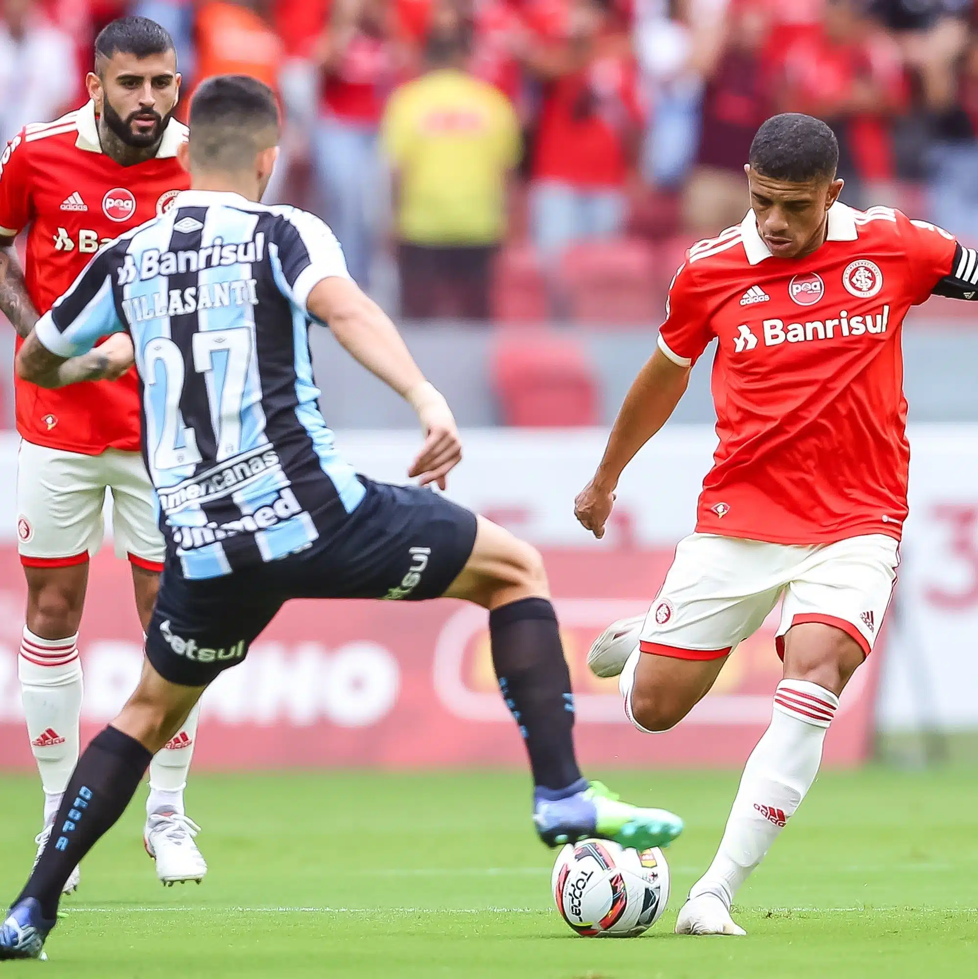 Jogadores do grêmio e do Inter disputando a bola em campo.