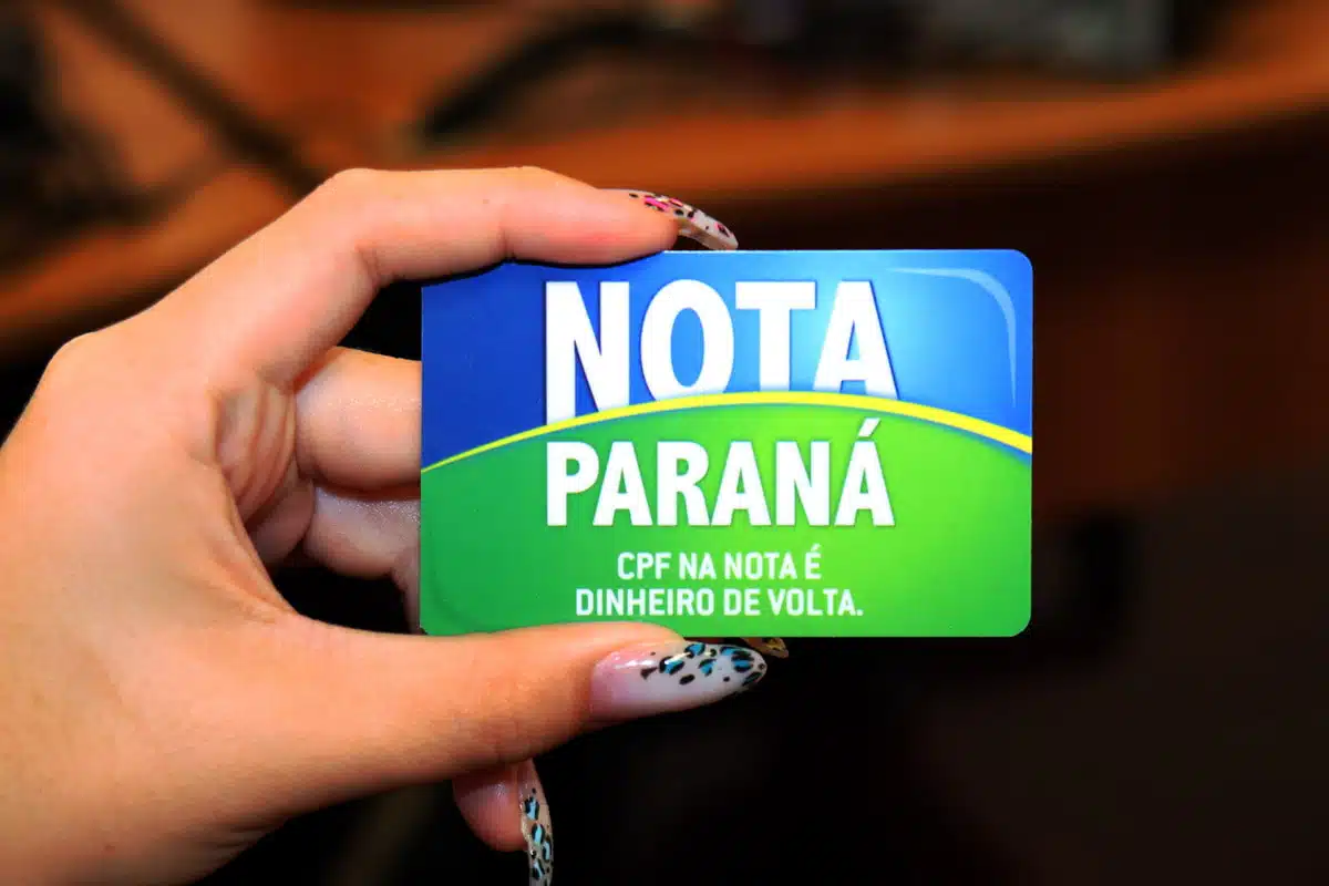 Na imagem, uma mão feminina segurando o cartão do Nota Paraná