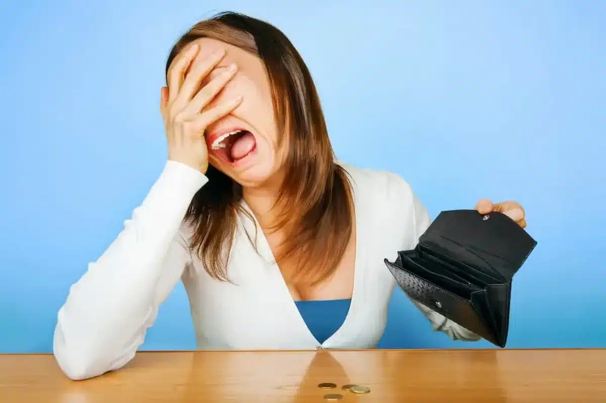 Imagem mostra mulher chorando e segurando carteira sem dinheiro.