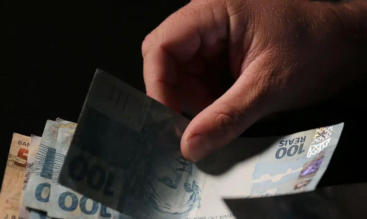 Foto mostra pessoa segurando nota de R$ 100. Imagem representativa do dinheiro gasto na Argentina.