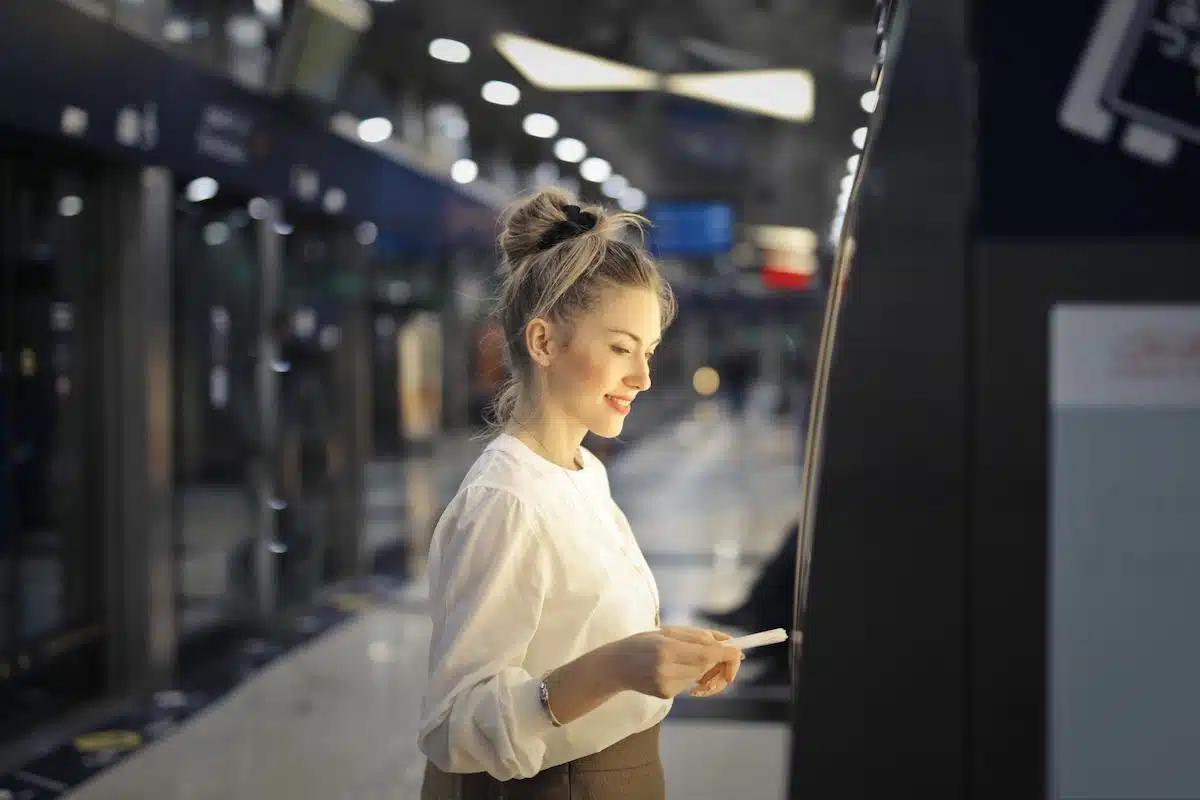 Foto mostra mulher sacando dinheiro em um caixa eletrônico de banco.