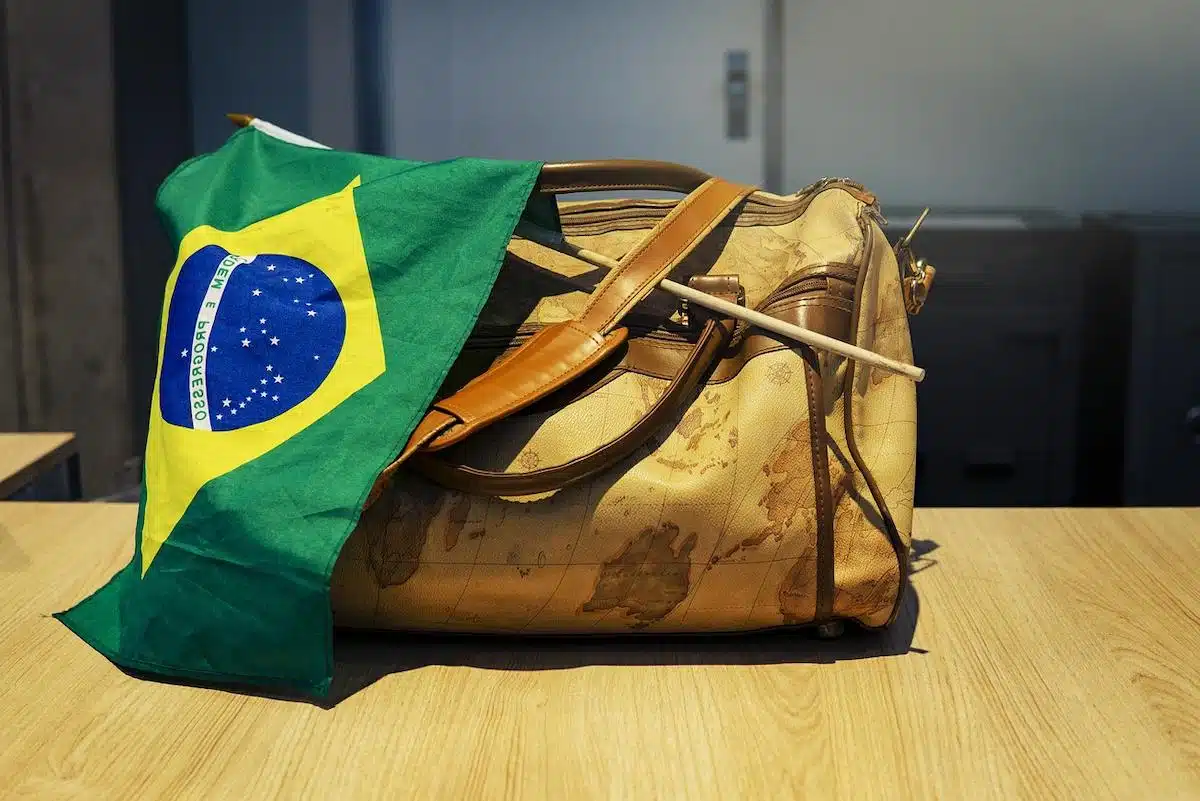 Foto mostra bandeirinha do Brasil apoiada em bagagem estampada com mapa.