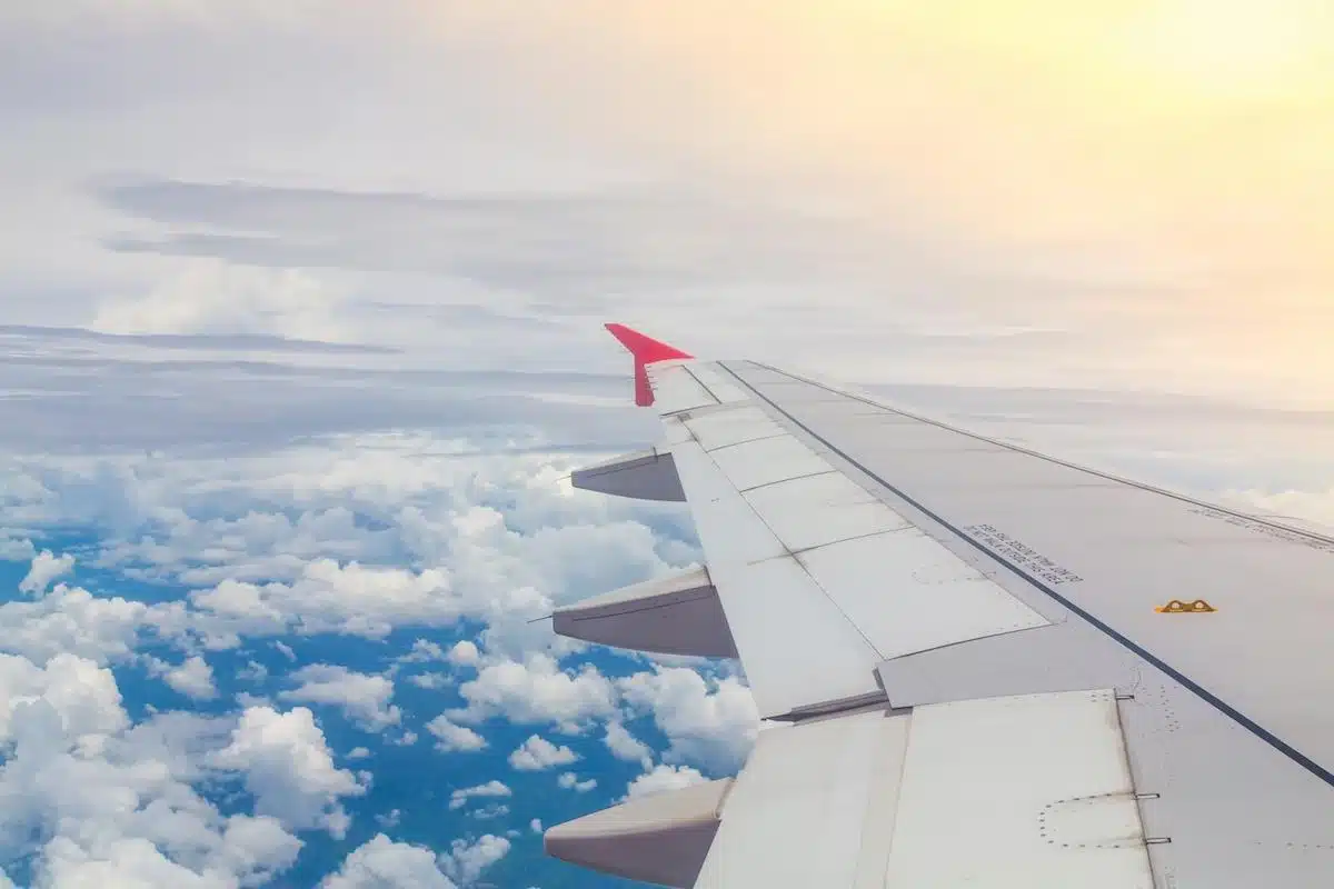 Foto mostra vista externa de um avião, da perspectiva de alguém que está de dentro - mostrando assim a asa e o horizonte, repleto de nuvens.