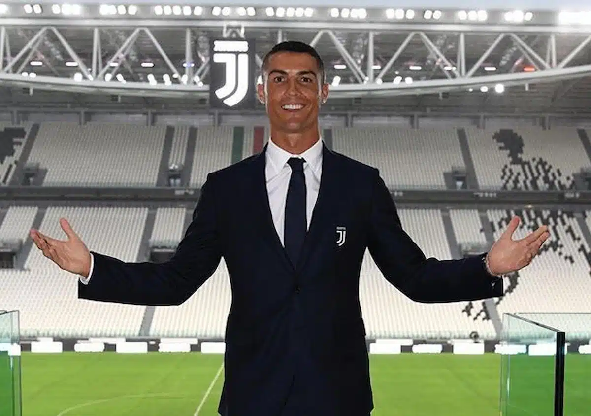 Foto mostra o jogador Cristiano Ronaldo, vestindo terno, frente a um campo de futebol.