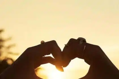 Foto mostra duas mãos fazendo gesto de amor, em um pôr do sol. Imagem ilustrativa do amor que pode ser encontrado por pessoas de certos signos.