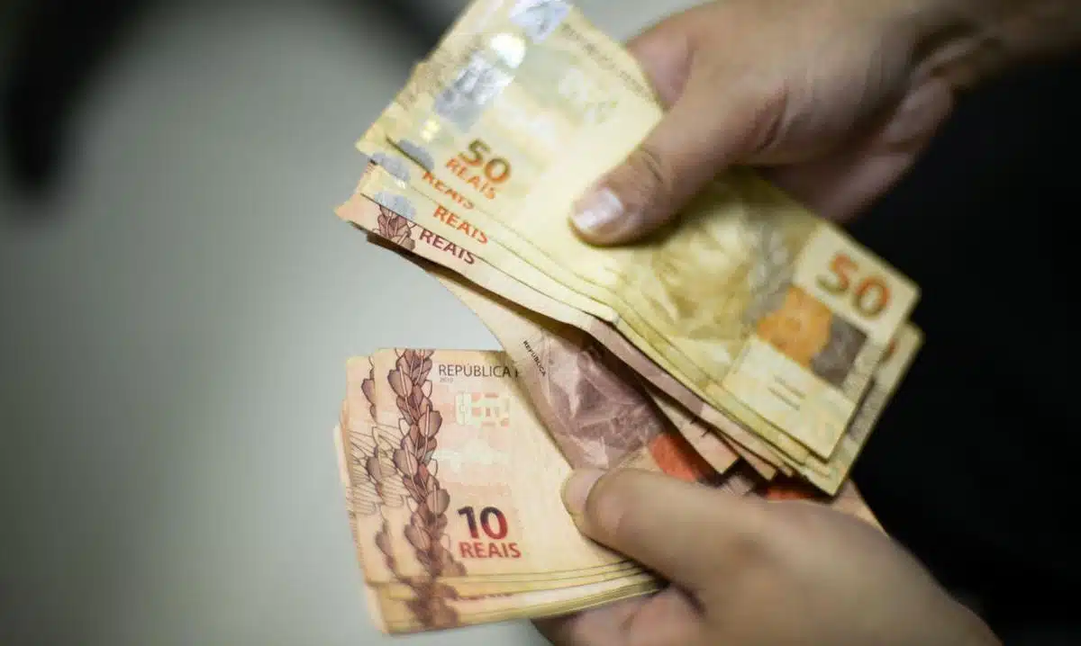 Foto mostra mãos de uma pessoa segurando cédulas de real, algumas de R$ 50 e outras de R$ 10. Imagem ilustrativa dos pagamentos do programa Nota Fiscal Gaúcha.