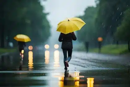 Imagem mostra pessoa caminhando na chuva com guarda-chuva amarelo.