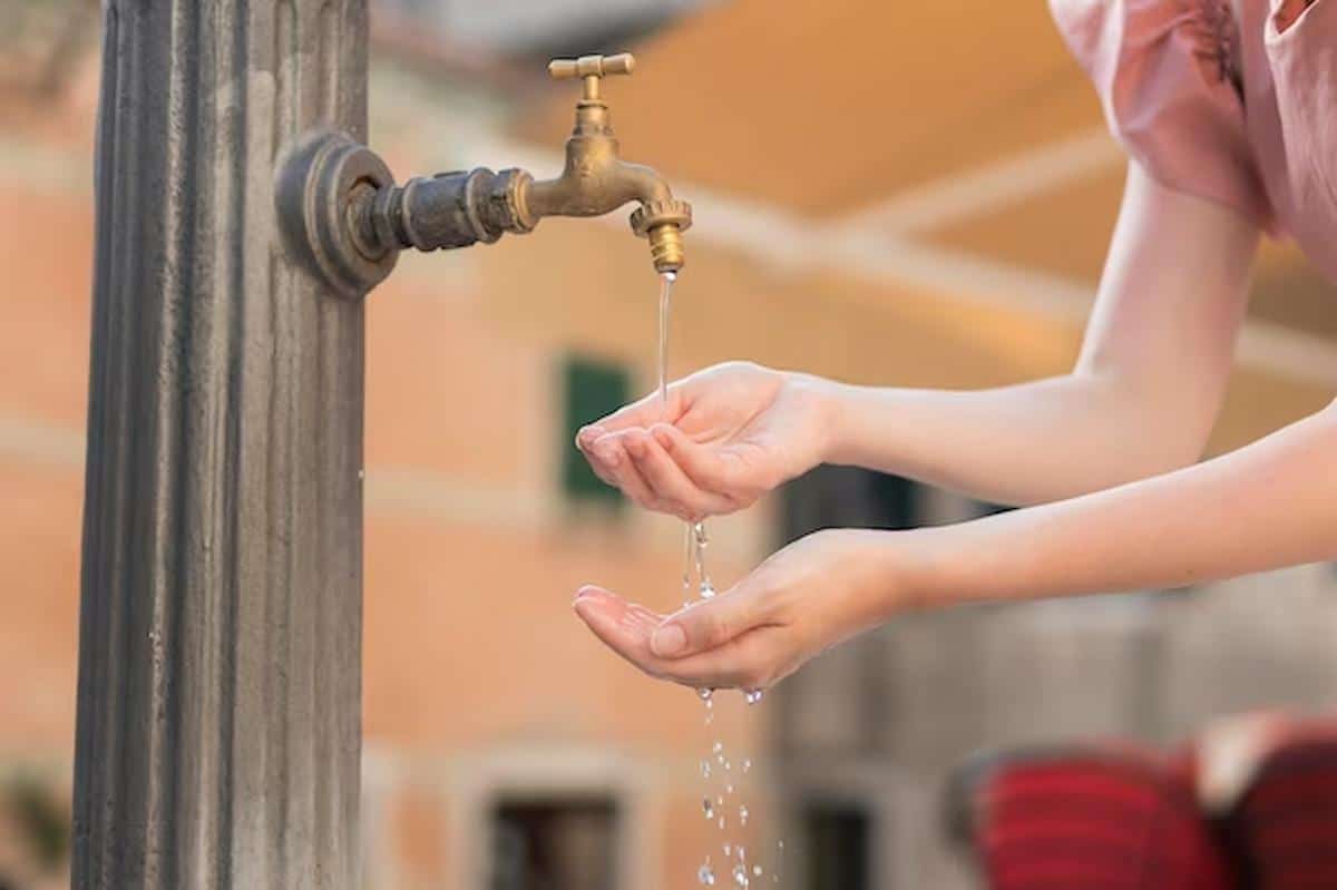 Foto mostra pessoa abrindo torneira, lavando as mãos com água.