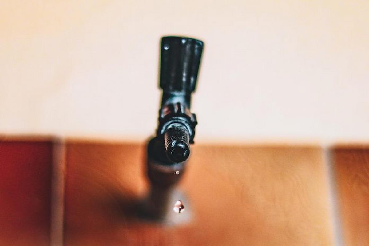 Foto mostra torneira preta pingando água, frente à uma parede bege.