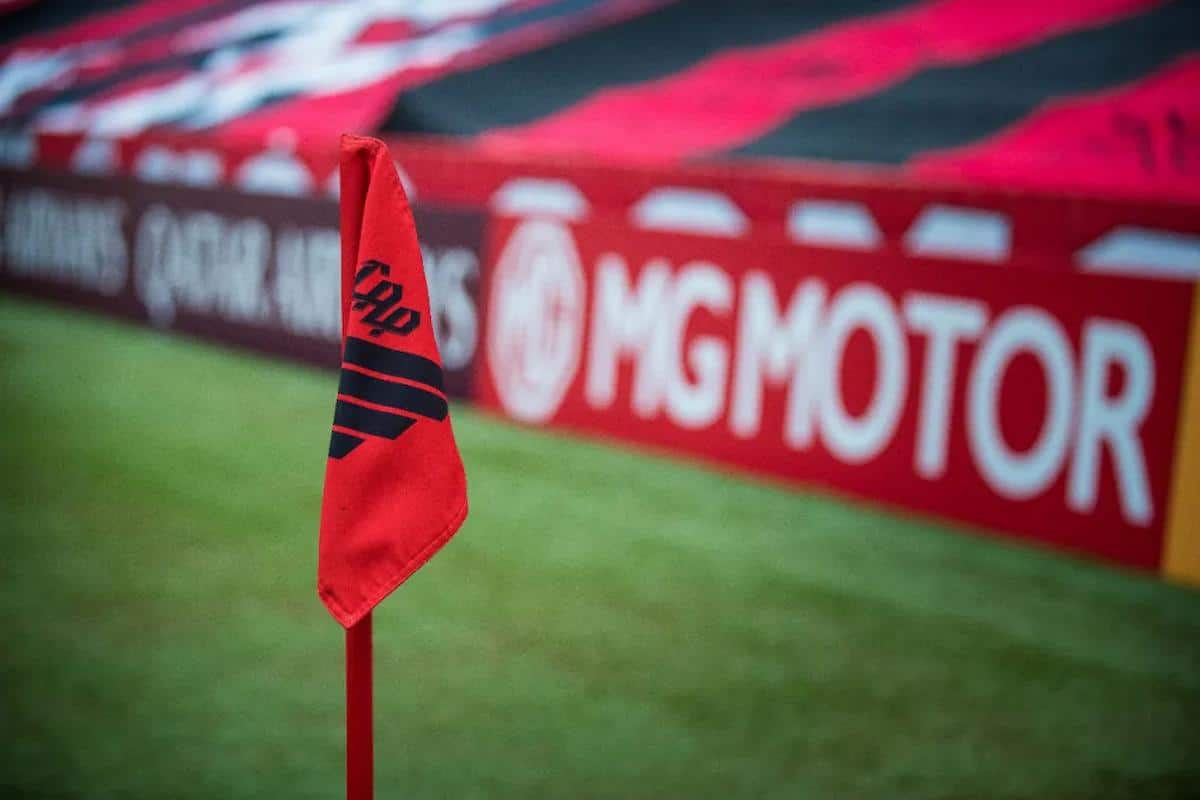 Foto mostra bandeira representativa do clube do Athletico-PR em um campo de futebol.