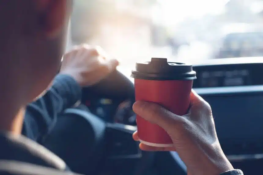 Homem dirigindo carro enquanto segura um copo de café.