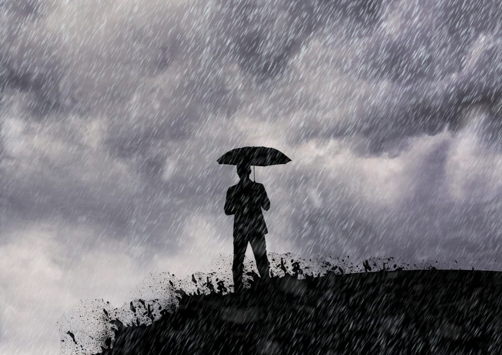 Na imagem, uma pessoa em um morro com um guarda chuva, enquanto chove bastante