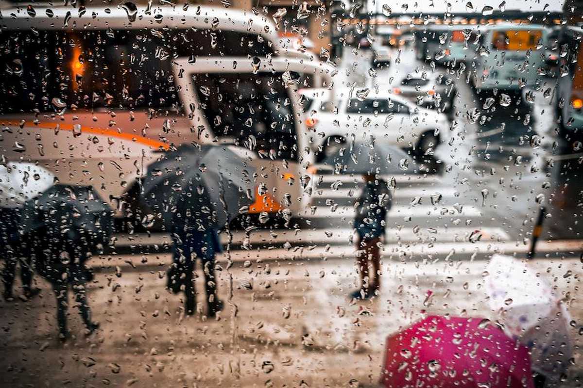 A foto mostra pessoas em rua durante momento de chuva, próximo ao trânsito. Imagem ilustrativa das tempestades que podem atingir o RS.