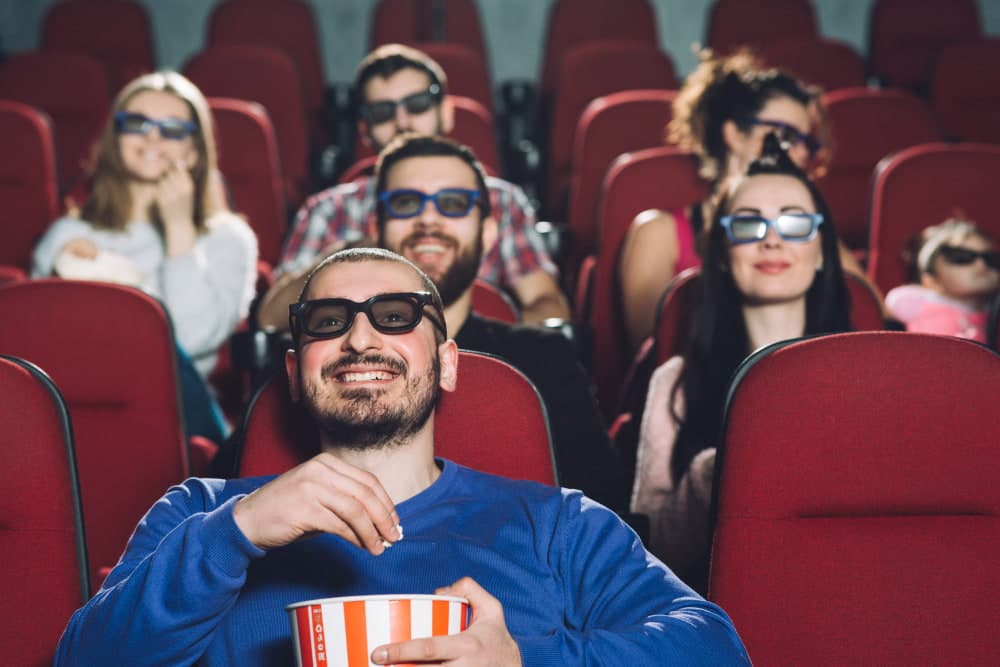 Na imagem, pessoas rindo em uma sala de cinema