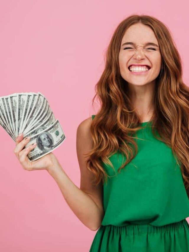 Foto mostra mulher segurando cédulas de dólar, em estado de felicidade. Imagem ilustrativa da riqueza que pode ser alcançada por determinados signos em agosto.