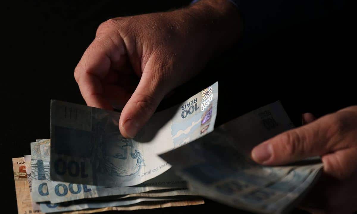 Foto mostra pessoa segurando notas de dinheiro em um ambiente escuro.