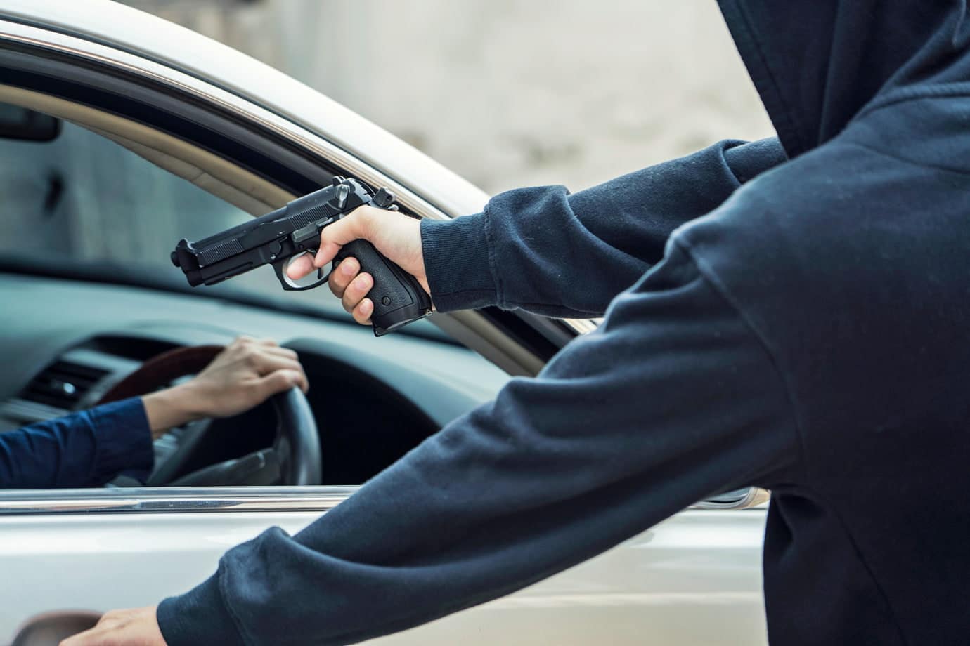 Na imagem, uma pessoa apontando uma arma para outra pessoa dentro de um carro