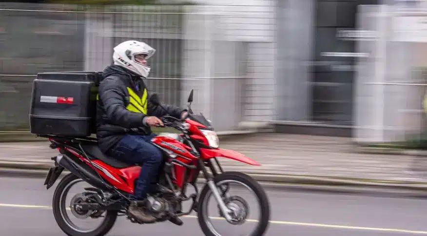 Na imagem, um motoboy dirigindo sua moto