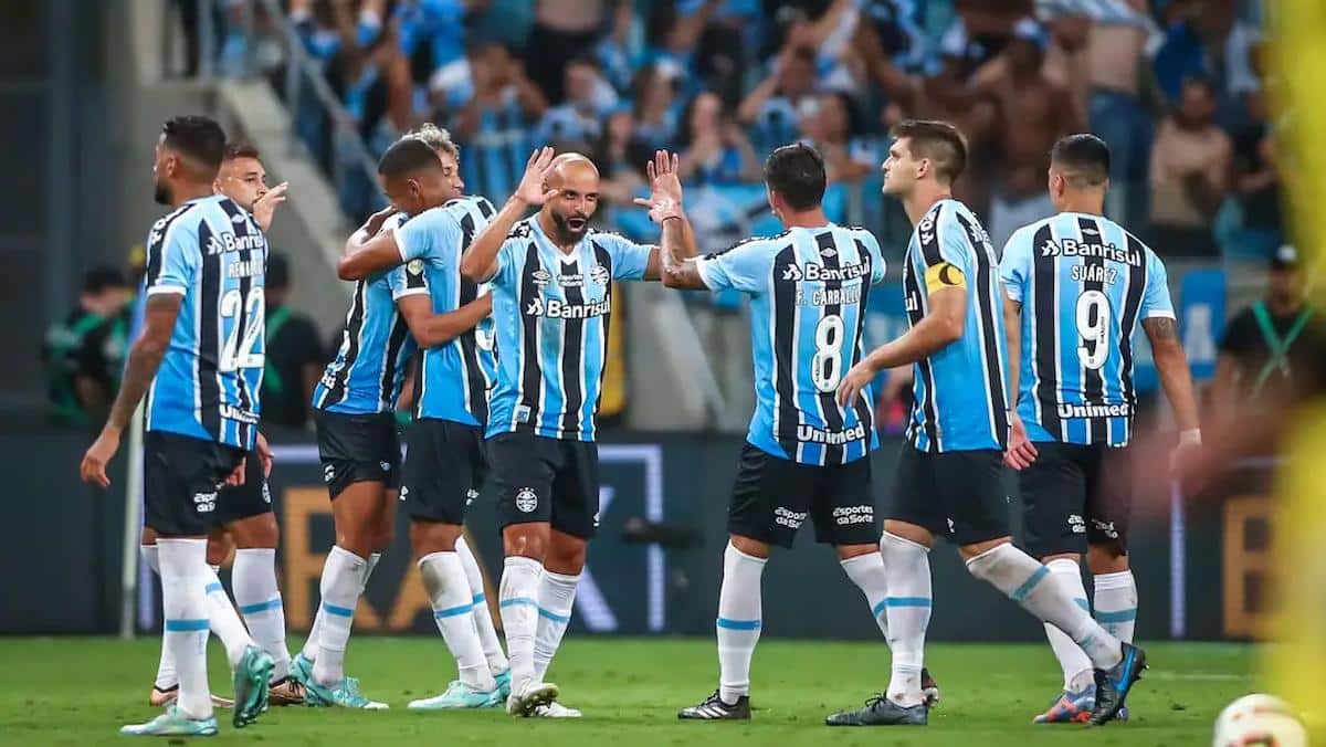 Foto mostra equipe do Grêmio reunida em um gramado de futebol.