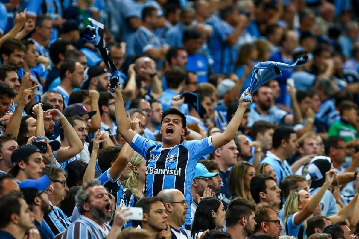 Foto mostra torcida do Grêmio em arquibancada.