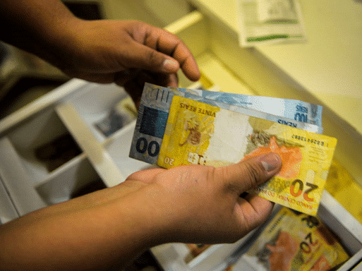 Imagem de pessoa segurando notas de 20 e 100 reais, ilustrativa da integração de moeda entre Brasil e Argentina.
