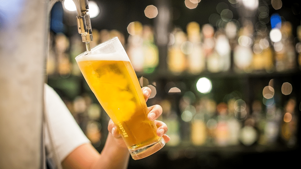 Imagem de pessoa enchendo copo de cerveja em ambiente de bar.