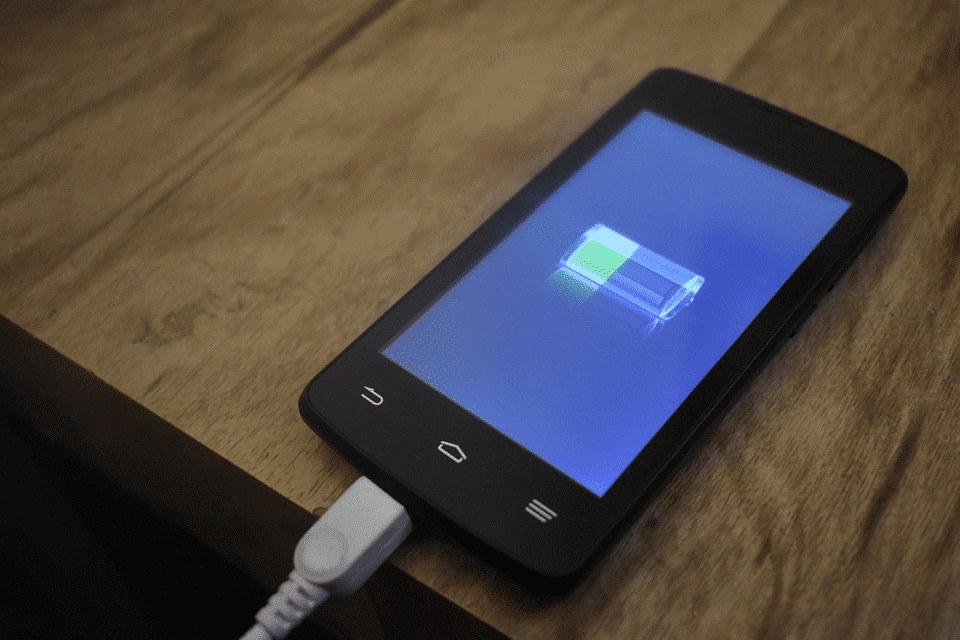 Imagem mostra celular carregando em cima de mesa.