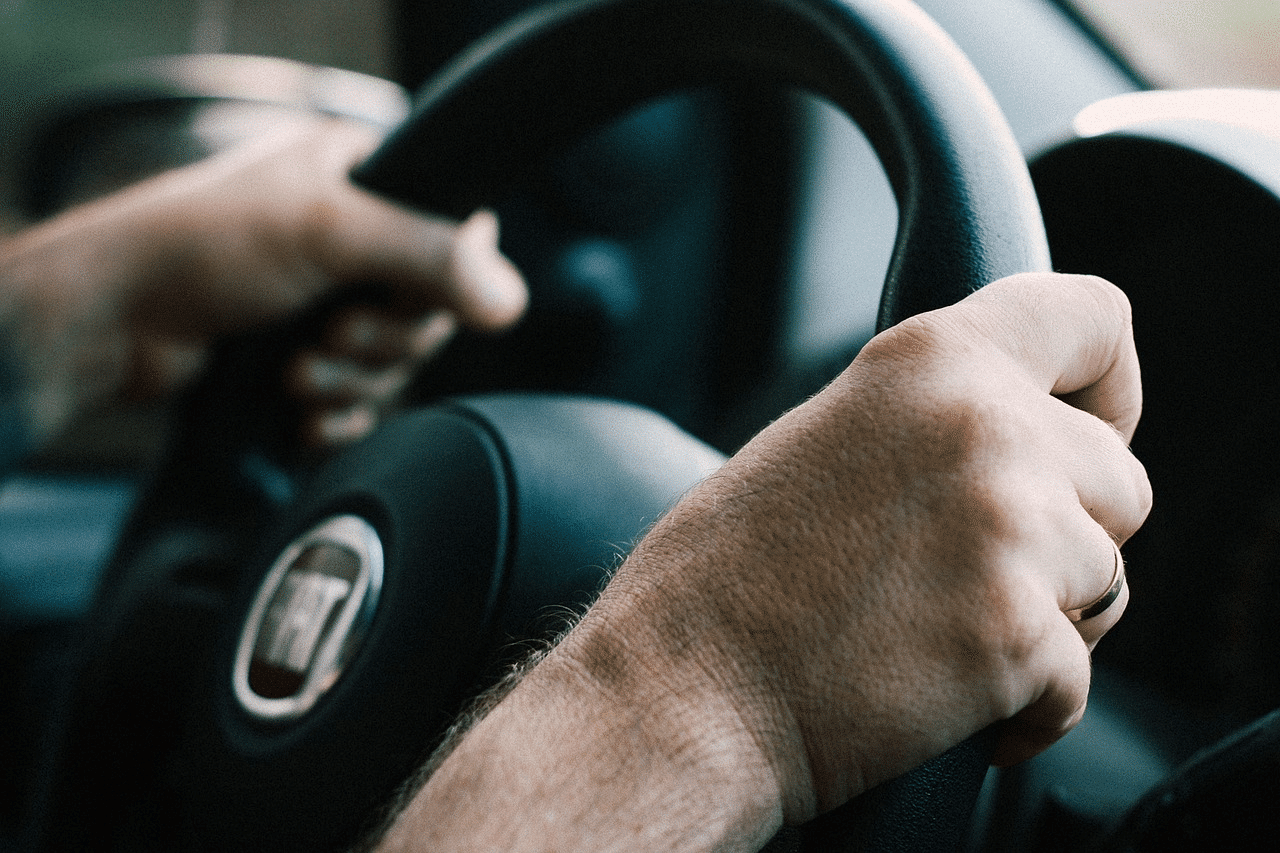 Foto mostra mãos de pessoa segurando volante de carro. A imagem é ilustrativa da possível redução da idade mínima para tirar a CNH.