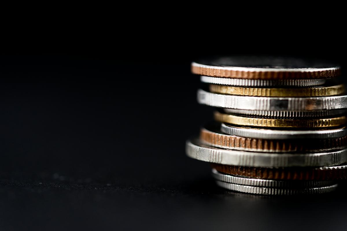 Foto mostra pilha de moedas em um fundo escuro.
