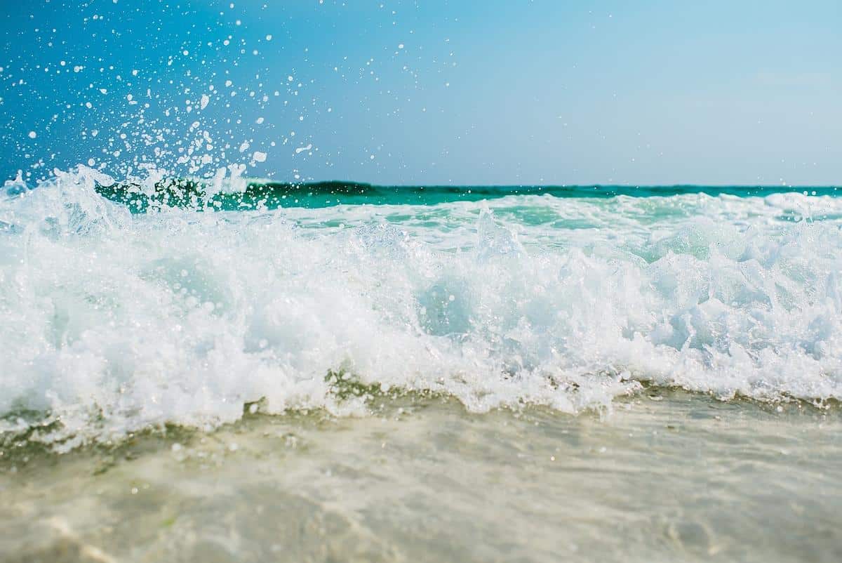 Foto mostra ondas quebrando na areia em uma praia.
