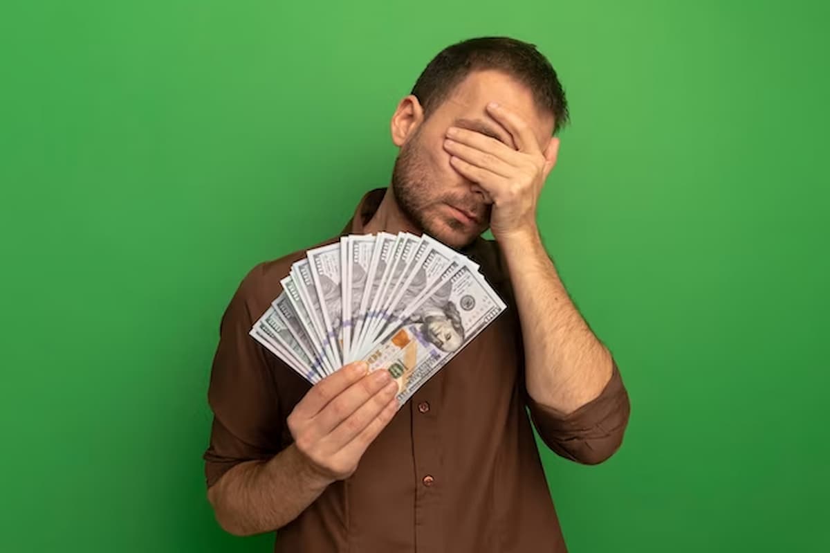 Imagem mostra homem fechando os olhos e com notas de dinheiro na mão.