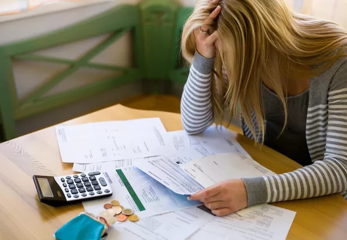 Imagem mostra mulher apoiada em mesas cheia de papéis e com uma calculadora, representando as dívidas de uma empresa de SC