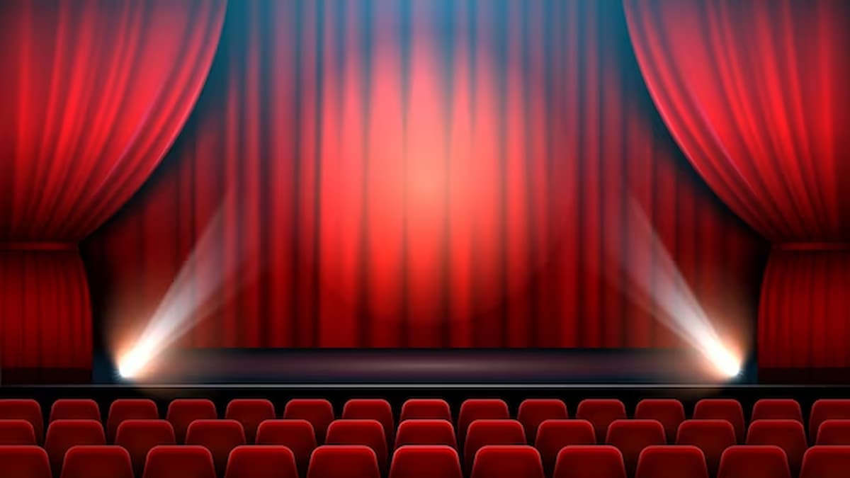 Interior do palco do espetáculo de teatro com cortina vermelha, holofote e cadeiras de teatro.
